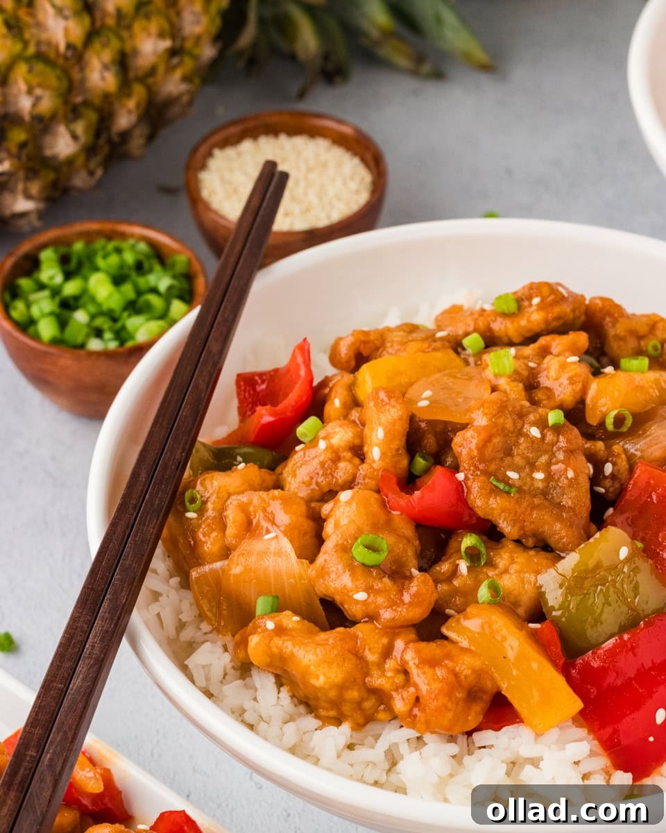 A vibrant plate of gluten-free sweet and sour chicken, garnished with fresh cilantro and sesame seeds, served alongside fluffy white rice. The chicken pieces are coated in a glossy, rich sauce, and slices of colorful bell peppers are visible.