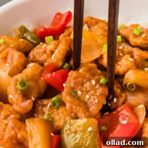 A close-up shot of chopsticks delicately picking up a piece of perfectly glazed sweet and sour chicken, highlighting the rich texture and vibrant colors of the dish.