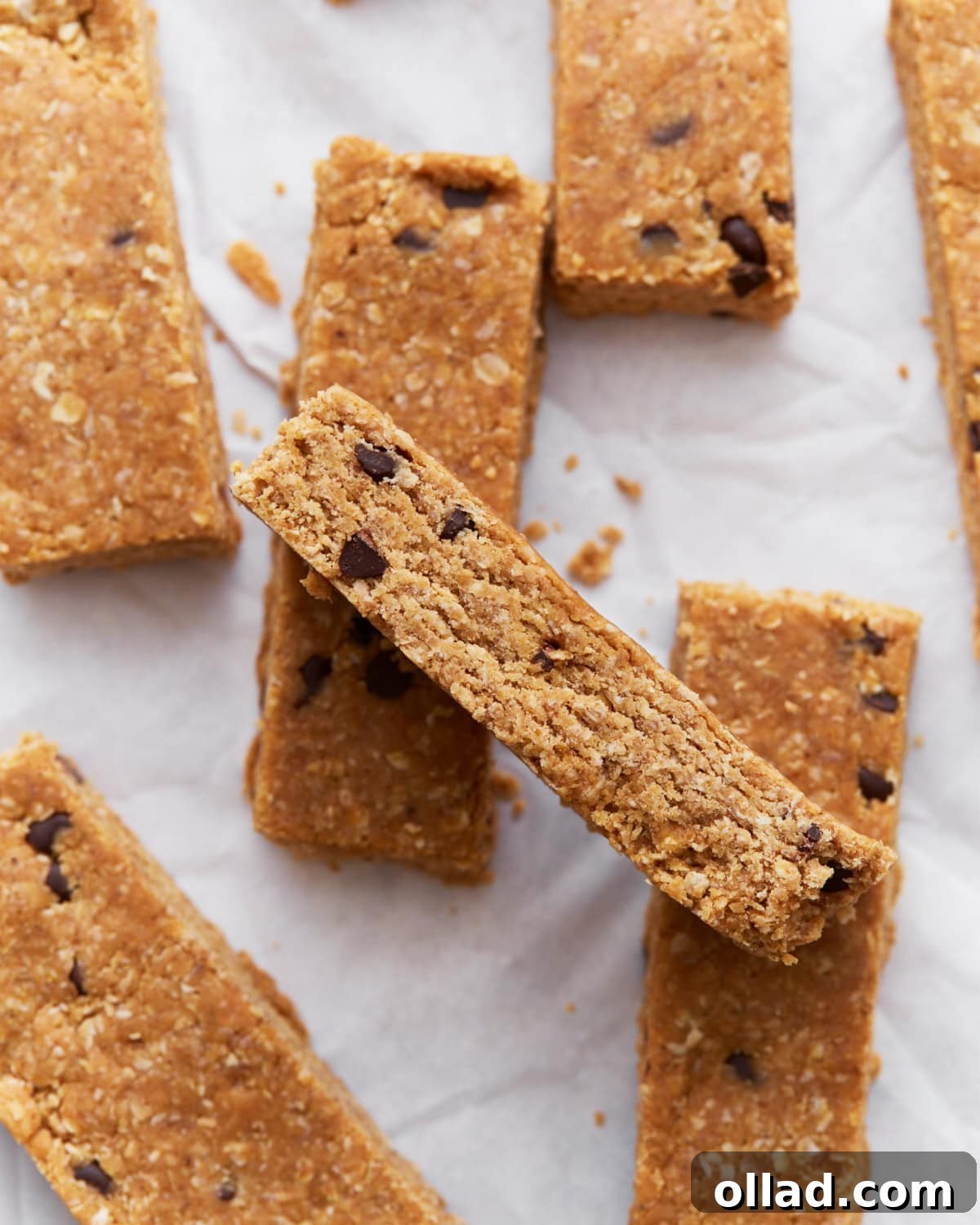 Simple & Delicious Homemade Gluten-Free Granola Bars 2 Homemade gluten-free granola bars stacked on parchment paper, showing their golden brown texture and chocolate chip details.