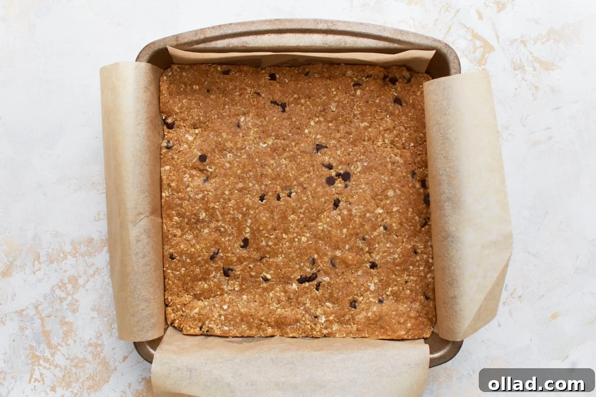 Simple & Delicious Homemade Gluten-Free Granola Bars 7 Pressed gluten-free granola bar mixture in a parchment-lined baking dish, flattened evenly with a measuring cup.