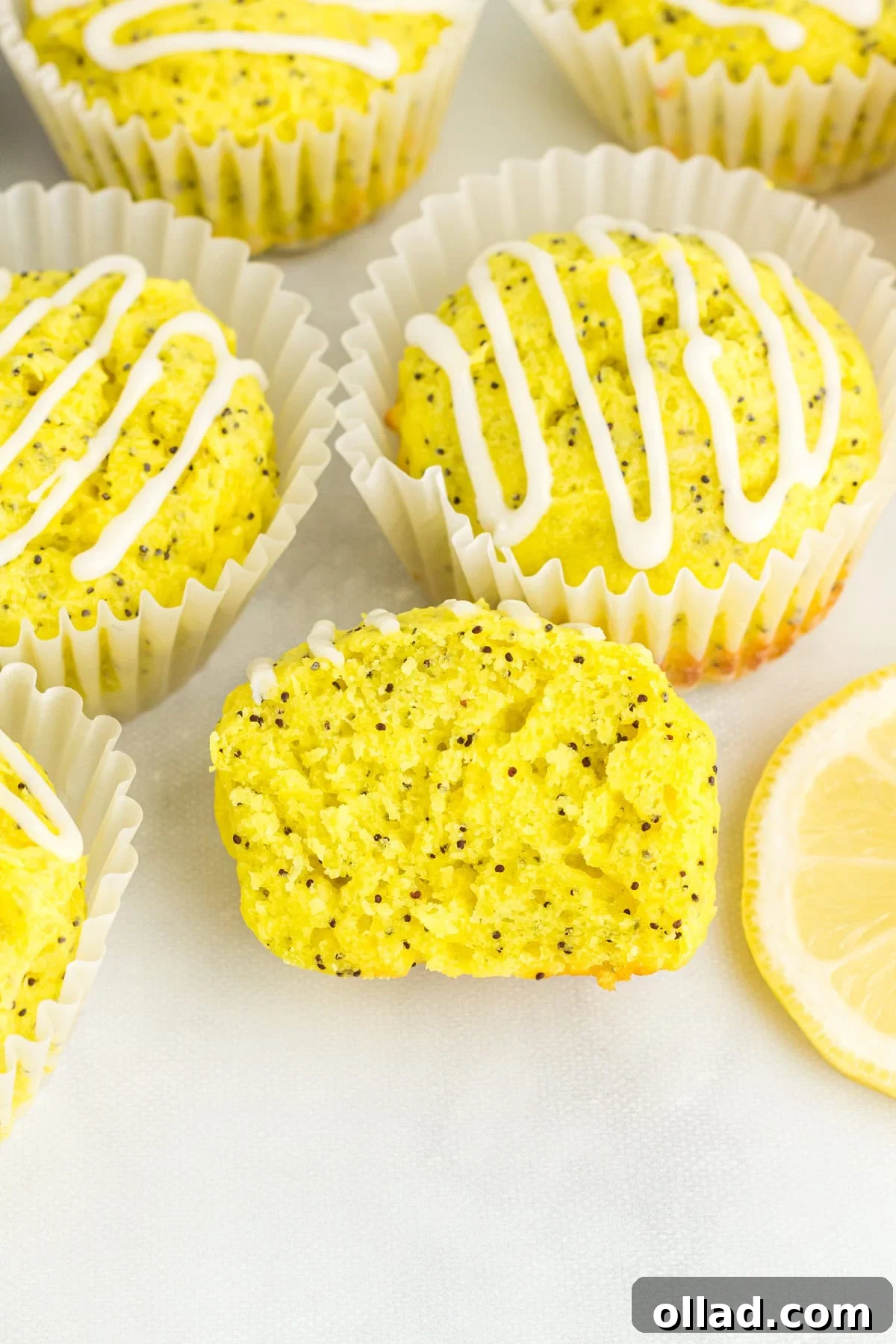 Tangy & Tender Gluten-Free Lemon Poppy Seed Muffins 2 Soft, moist gluten-free lemon poppy seed muffins with a vibrant lemon glaze, arranged in white paper liners, with one muffin sliced to reveal its tender crumb and poppy seeds.