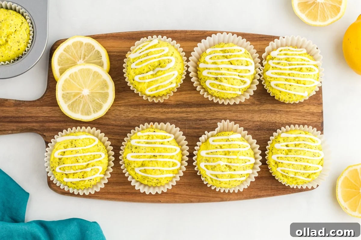 Tangy & Tender Gluten-Free Lemon Poppy Seed Muffins 11 Gluten-free lemon poppy seed muffins, beautifully topped with white lemon glaze, arranged on a wooden board with fresh lemon slices as garnish.