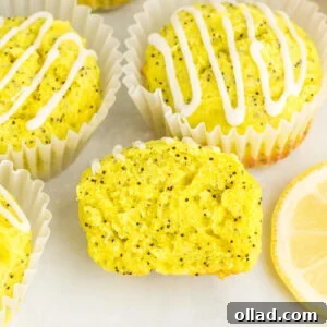 Gluten-free lemon poppy seed muffins with lemon glaze in white liners, one muffin sliced open to show moist crumb and poppy seeds