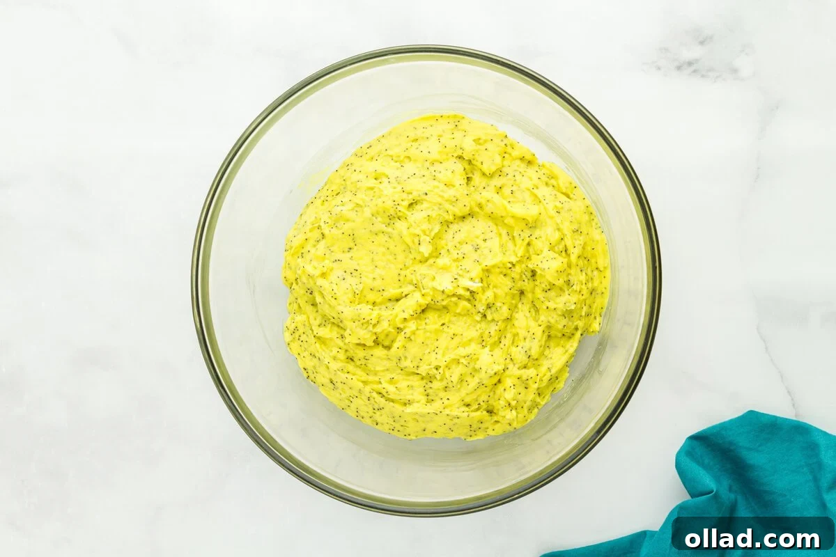 Tangy & Tender Gluten-Free Lemon Poppy Seed Muffins 7 Thick, bright yellow gluten-free lemon poppy seed muffin batter, showing visible poppy seeds, in a glass mixing bowl.