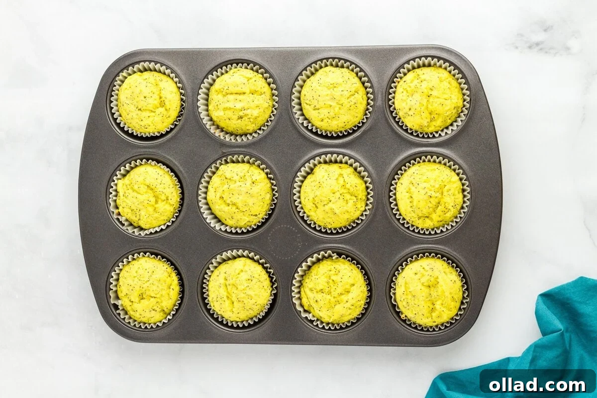 Tangy & Tender Gluten-Free Lemon Poppy Seed Muffins 9 Gluten-free lemon poppy seed muffin batter portioned evenly into white paper liners within a muffin tin, ready for baking.