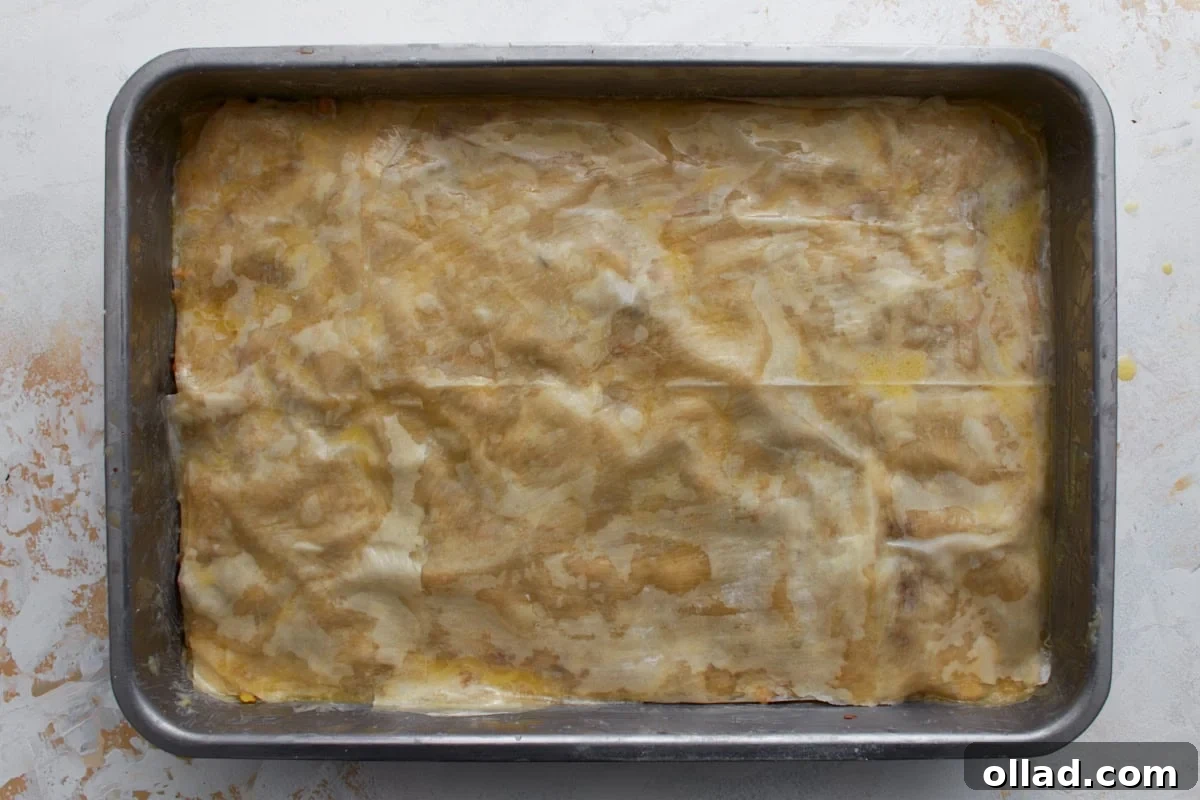 Final layer of butter-brushed gluten-free phyllo dough covering the baklava before baking.