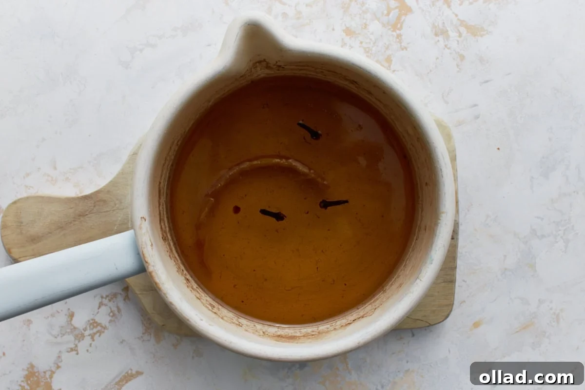 Honey syrup with whole cloves and lemon peel simmering in a small saucepan for gluten-free baklava.