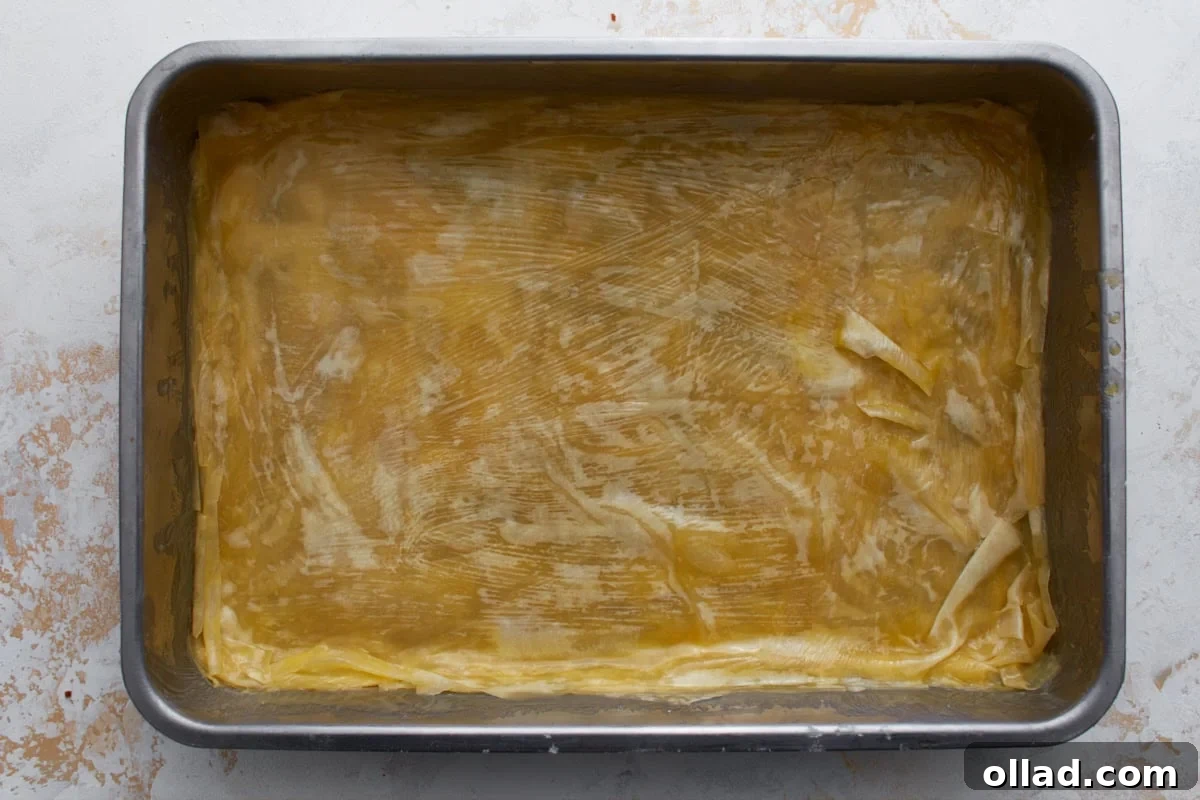 Butter-brushed gluten-free phyllo dough layered in a baking dish for homemade baklava.