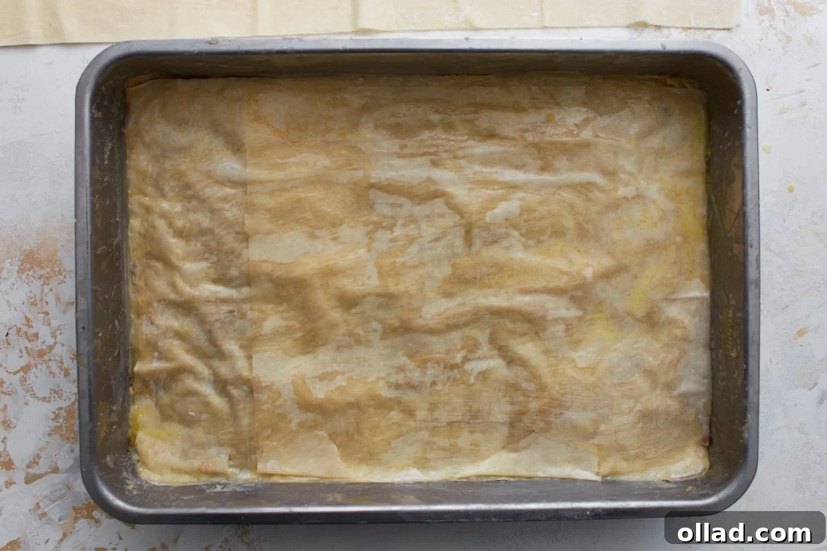 More buttered gluten-free phyllo sheets layered over the nut filling in a baking dish.