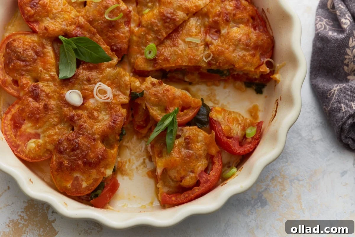 Crustless tomato pie sliced in a white baking dish with visible layers of tomatoes, basil, and melted cheese.