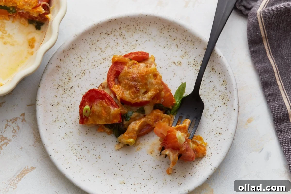 Slice of crustless tomato pie served on a plate with melted cheese, fresh tomatoes, basil, and green onions.
