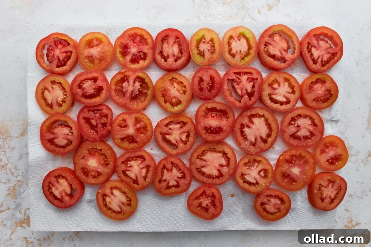 Sliced fresh tomatoes arranged on paper towels to drain excess moisture before making crustless tomato pie.
