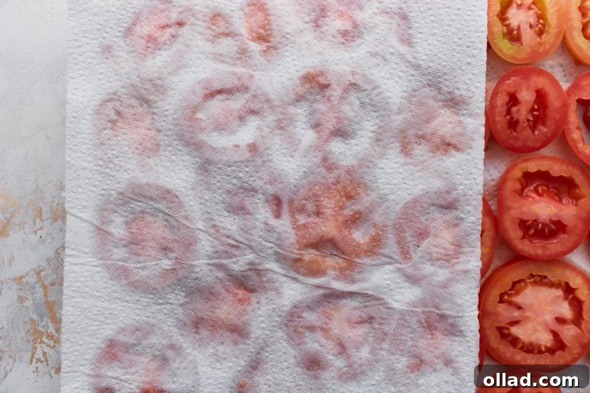 Paper towels pressed over sliced tomatoes to absorb excess moisture for crustless tomato pie.