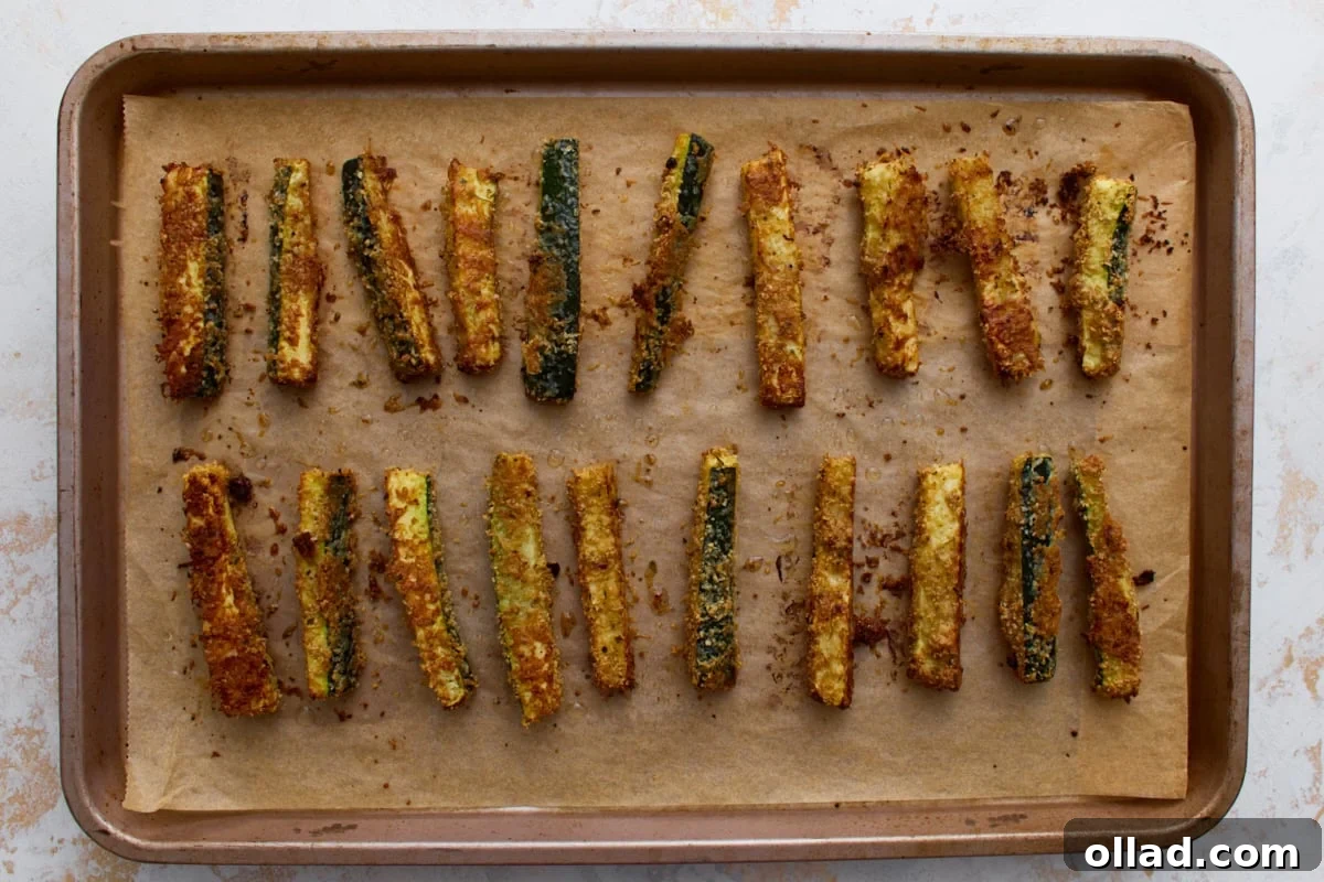 Crispy Keto Zucchini Fries: Low-Carb Snack Recipe 11 Golden brown baked keto zucchini fries on a parchment-lined baking sheet after roasting until crispy.