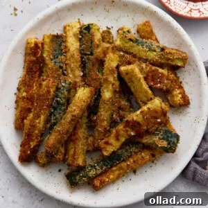 Crispy Keto Zucchini Fries: Low-Carb Snack Recipe 3 Crispy baked keto zucchini fries coated in Parmesan and almond flour served on a white plate with a side of ketchup.