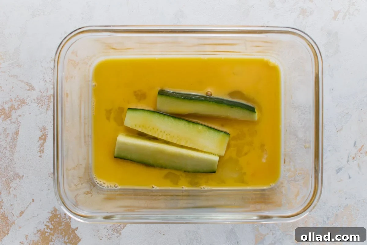 Crispy Keto Zucchini Fries: Low-Carb Snack Recipe 8 Zucchini sticks dipped in beaten egg before being coated in the Parmesan mixture.