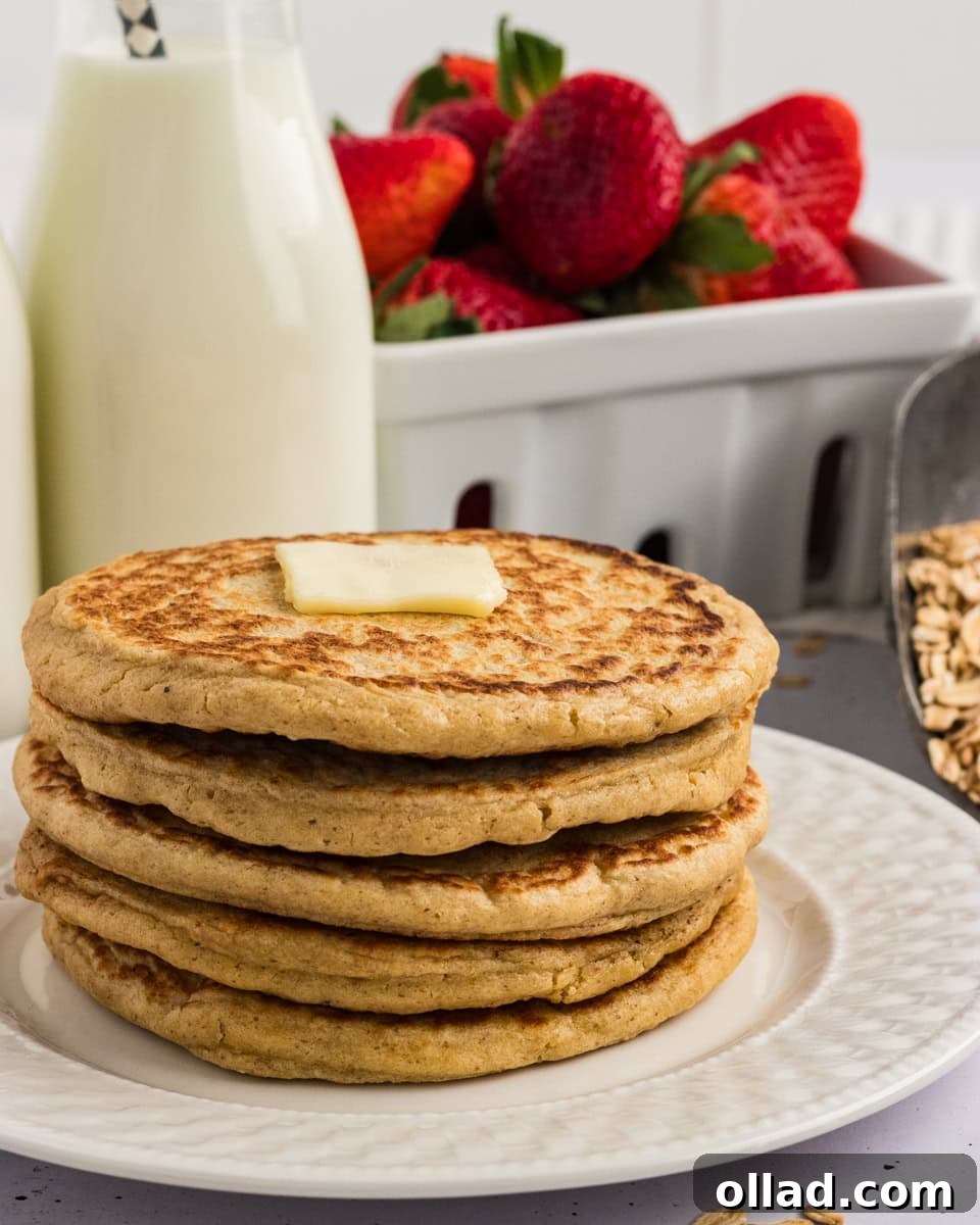Stack of oat flour pancakes topped with a pat of butter, served with fresh strawberries and a bottle of milk in the background.