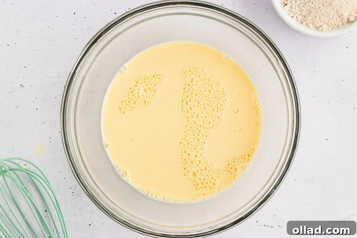 Milk, eggs, and vanilla whisked together in a glass bowl for oat flour pancake batter.