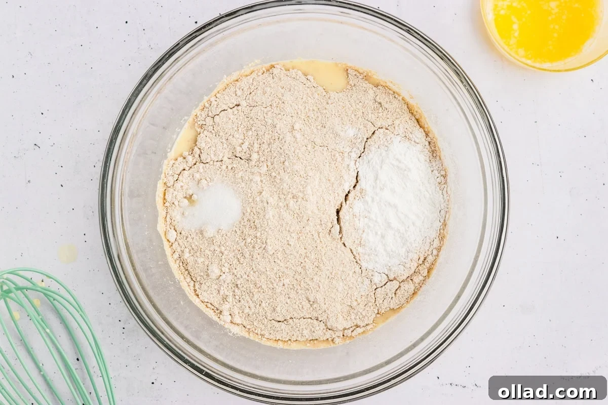 Oat flour, baking powder, and salt added on top of the whisked wet ingredients in a glass mixing bowl.