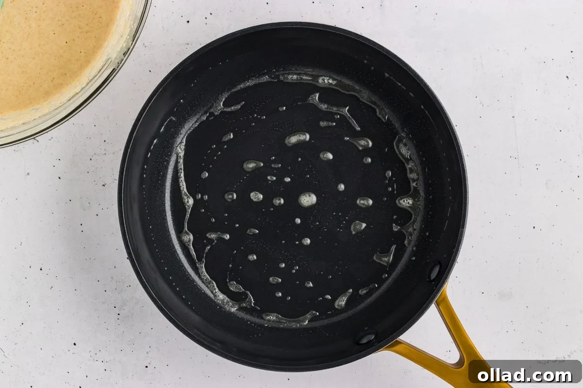 Melted butter coating a black skillet before cooking oat flour pancakes.