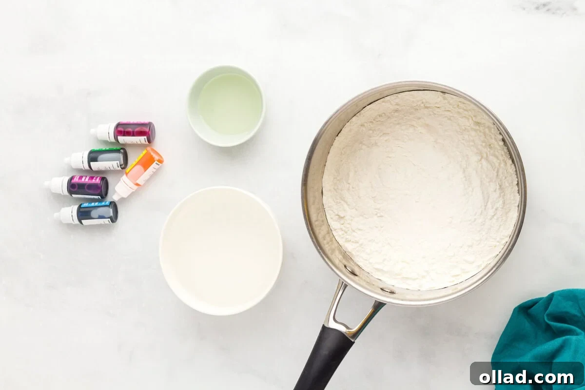 flour mixture in a pot with bowls of water and oil, and food coloring bottles nearby