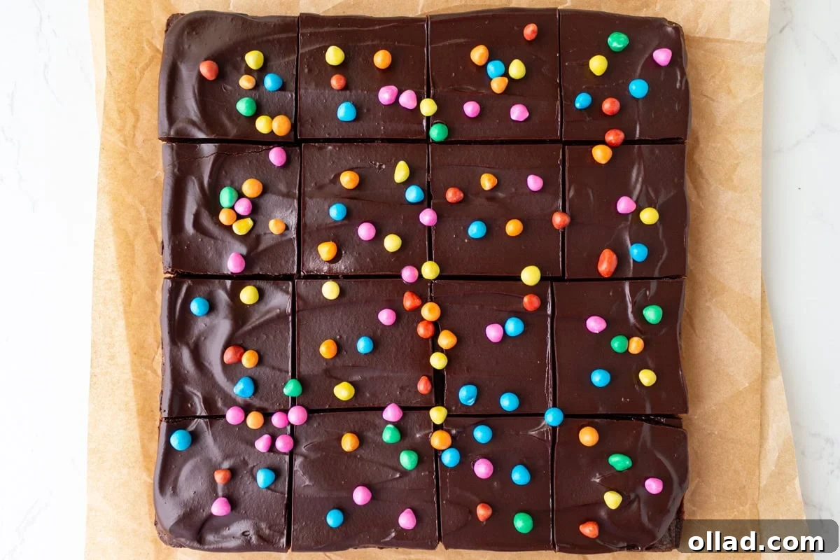 Frosted gluten-free cosmic brownies cut into squares and topped with rainbow candy chips on parchment paper.