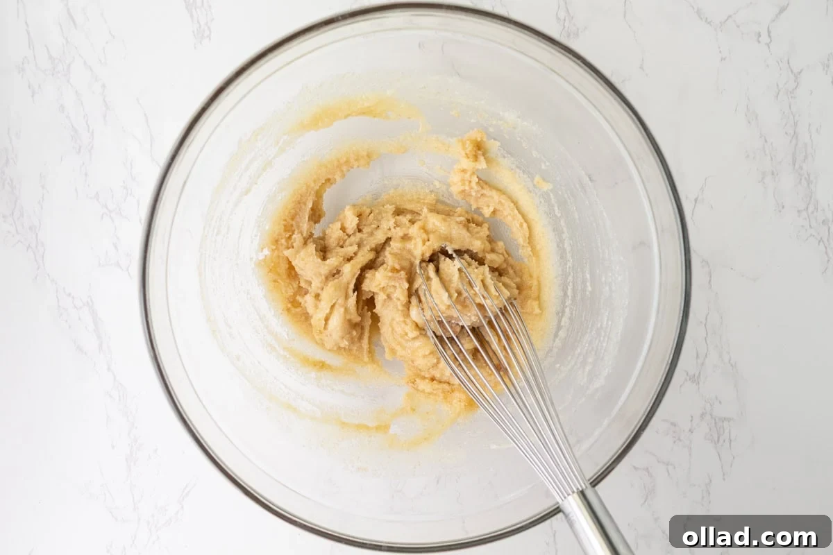 Melted butter whisked with granulated and brown sugar in a glass mixing bowl for gluten-free cosmic brownie batter.