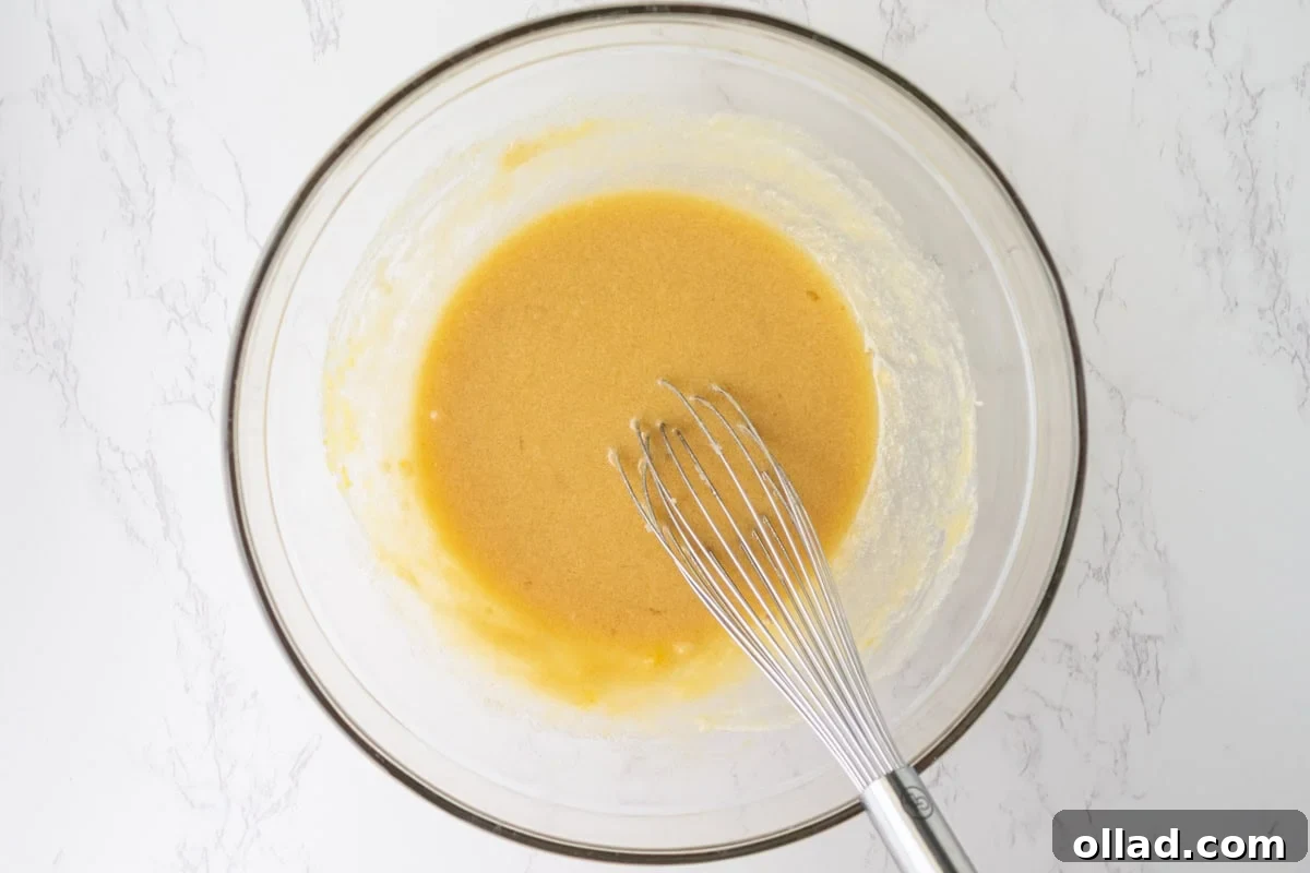 Eggs, corn syrup, and vanilla whisked into the butter and sugar mixture until glossy in a glass mixing bowl.
