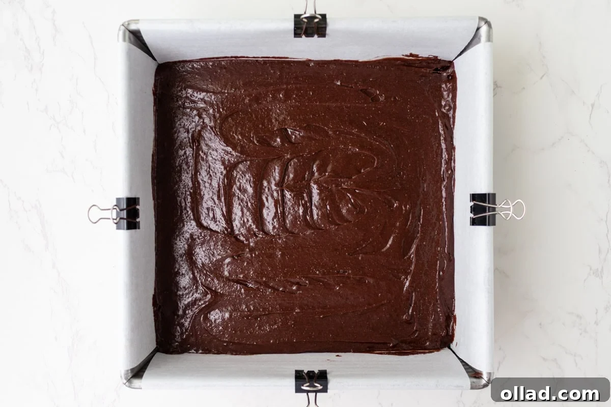 Gluten-free cosmic brownie batter spread into a parchment-lined 8x8 pan before baking.