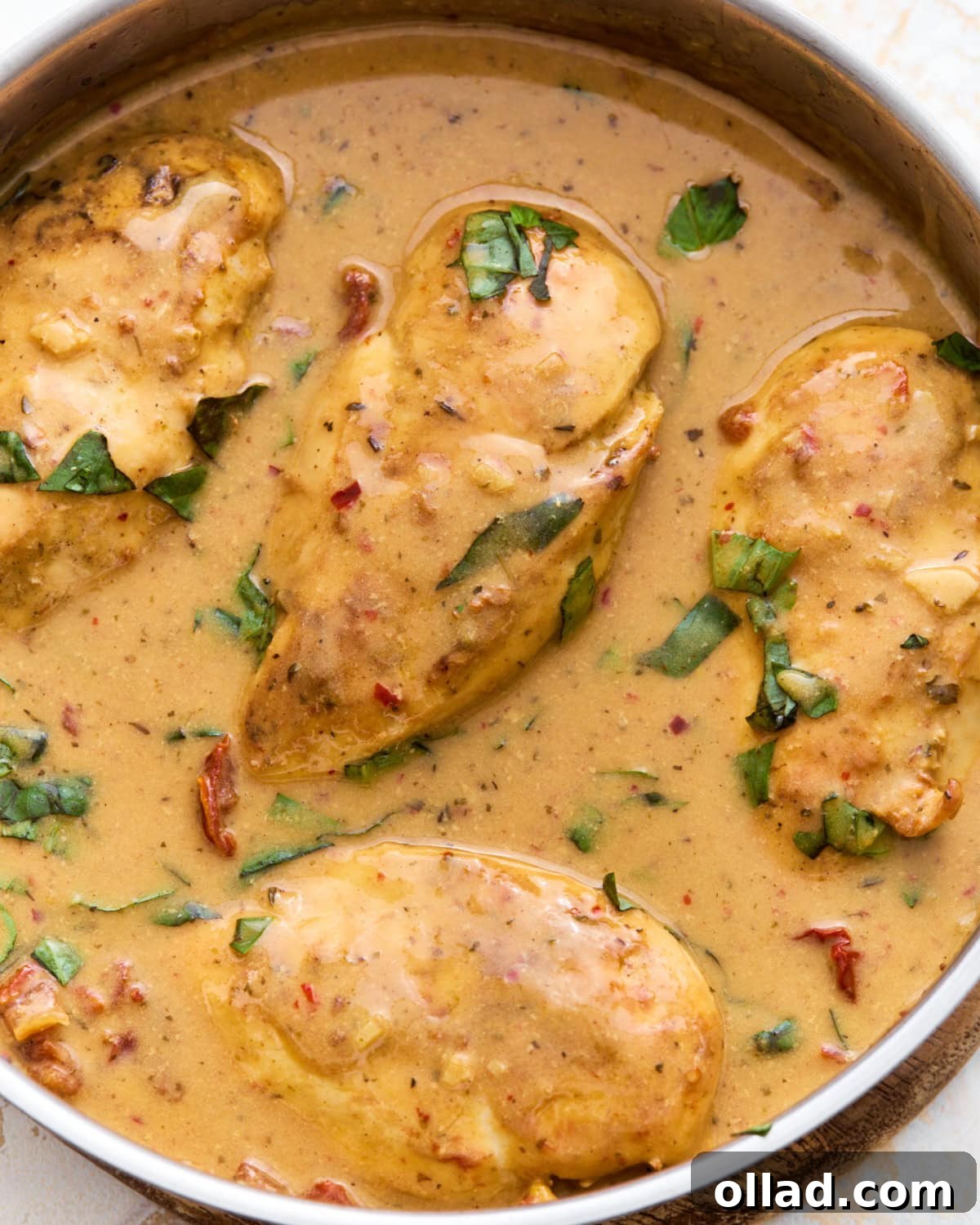 Overhead close-up of dairy-free Marry Me Chicken in a skillet, coated in a creamy sun-dried tomato sauce and topped with fresh basil.