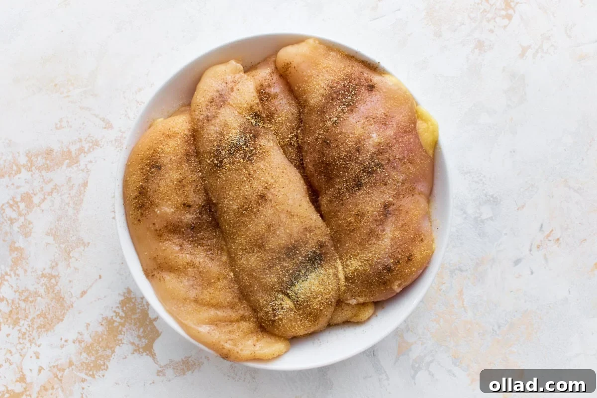 Raw chicken breasts seasoned with salt, pepper, and garlic powder in a white bowl, ready to sear for dairy-free Marry Me Chicken.