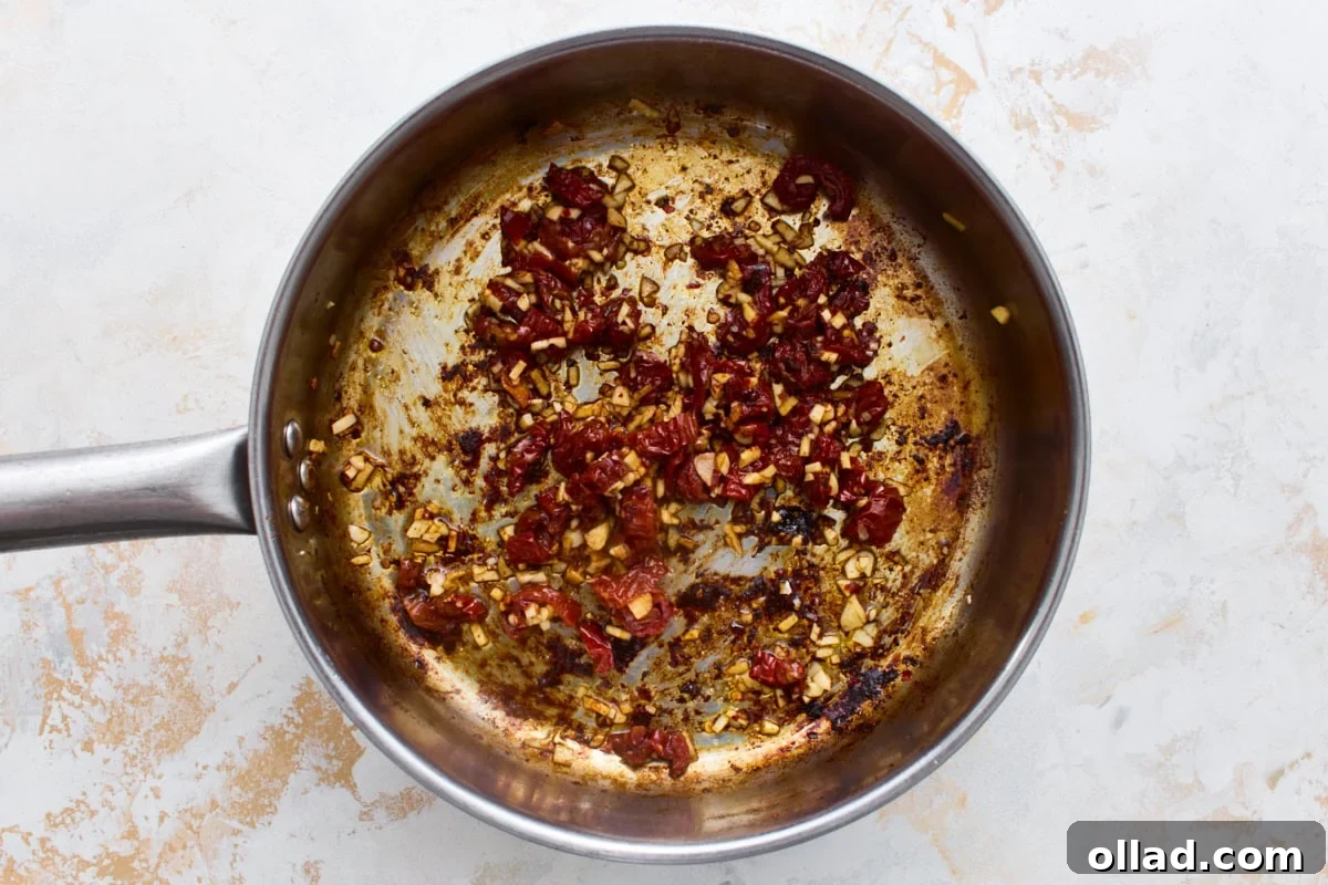 Minced garlic and chopped sun-dried tomatoes cooking in a skillet, the flavor base for dairy-free Marry Me Chicken sauce.