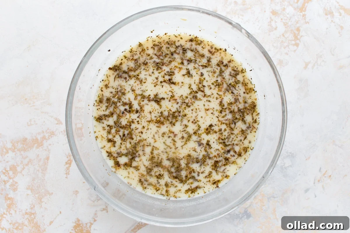 Chicken broth and coconut milk whisked together with nutritional yeast, cornstarch, and dried oregano in a glass bowl.