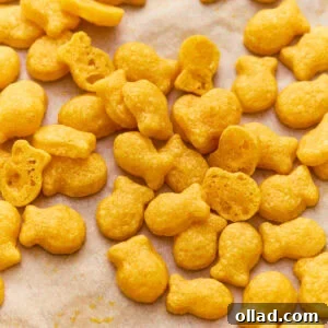 Gluten-free goldfish crackers scattered on parchment paper, with a few broken open to show the light, airy texture inside.