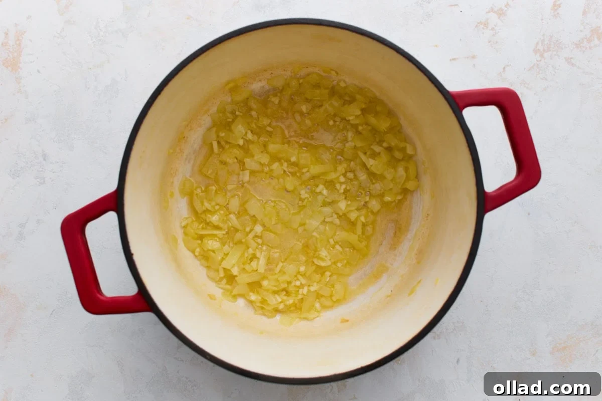 Softened, translucent onions and garlic cooking in butter in a red Dutch oven, the first step of gluten-free broccoli cheddar soup.