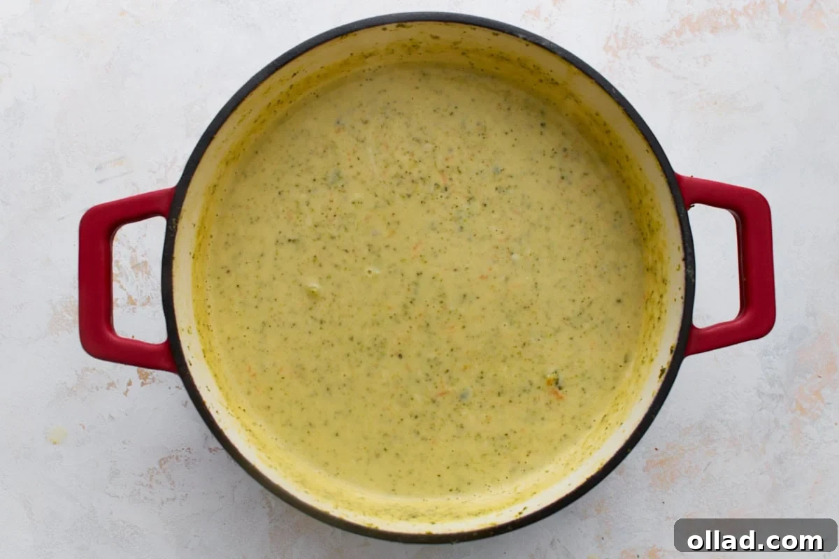Thick, smooth, glossy gluten-free broccoli cheddar soup in a red Dutch oven after the cheddar cheese has fully melted in.