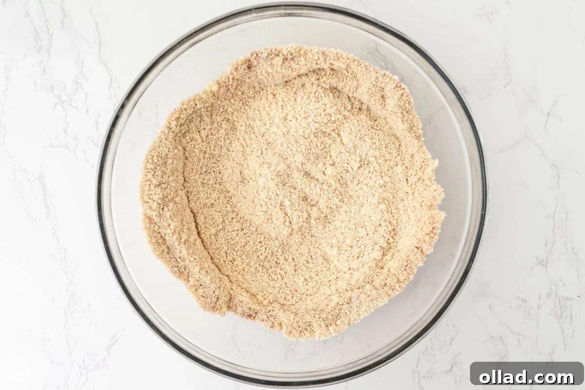 Almond flour and coconut flour whisked together with cinnamon, nutmeg, ginger, and cloves in a glass mixing bowl.