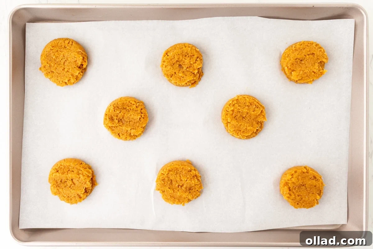 Scooped and flattened pumpkin cookie dough on a parchment-lined baking sheet before baking.