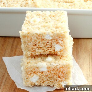 2 gluten-free rice krispies treats stacked with the pan of treats in the background