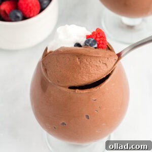 A glass filled with vegan chocolate mousse topped with whipped coconut cream and fresh berries