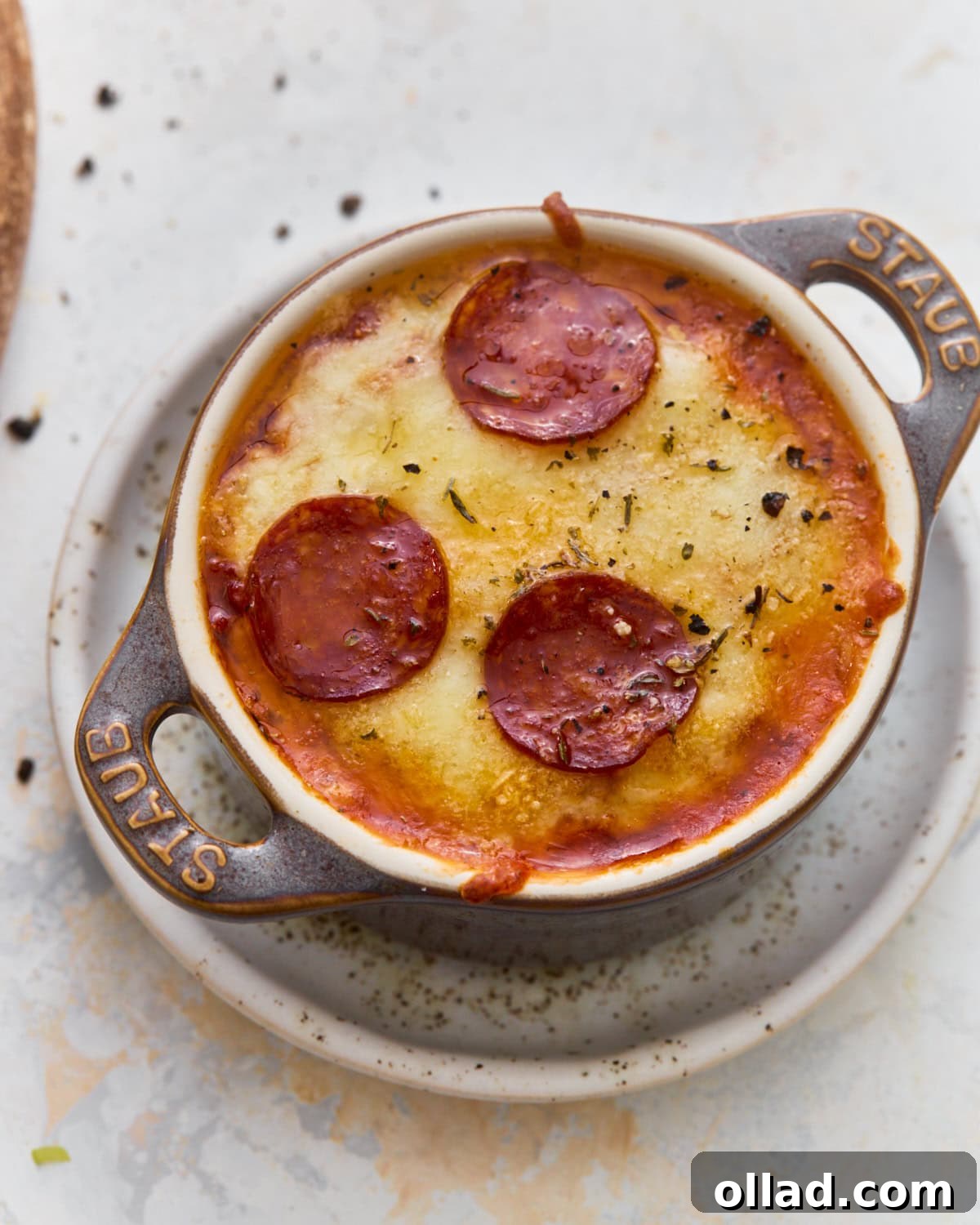 Overhead view of a gluten-free crustless pizza bowl with melted mozzarella, Parmesan, and pepperoni in a mini cast iron cocotte.