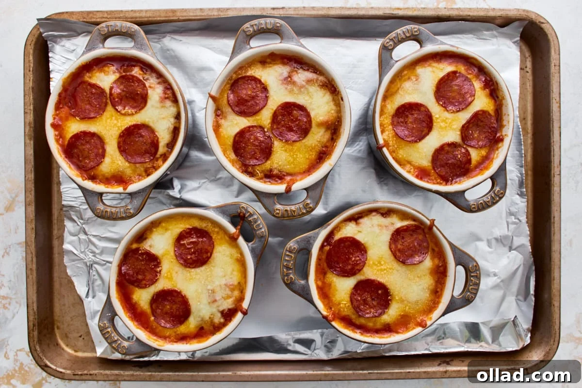 Five gluten-free crustless pizza bowls with melted, bubbly cheese on a baking sheet.