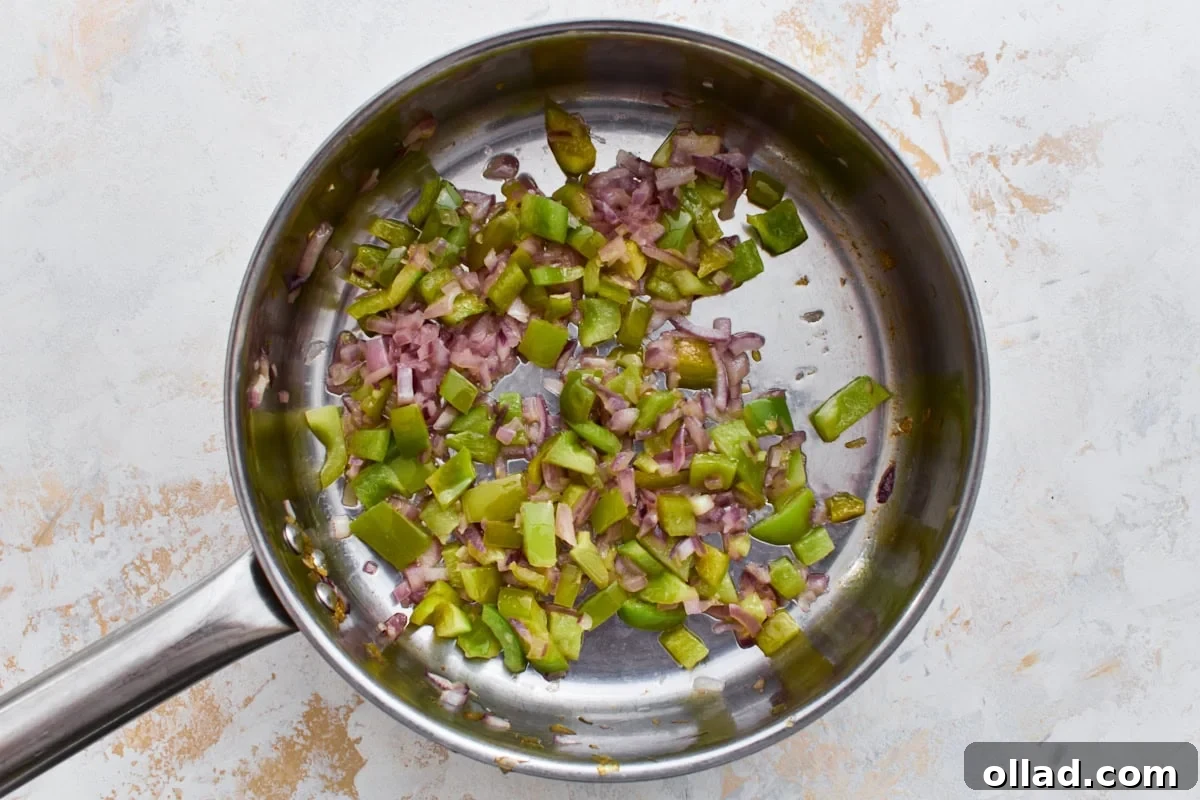 Diced red onion and green bell pepper cooking in a skillet.