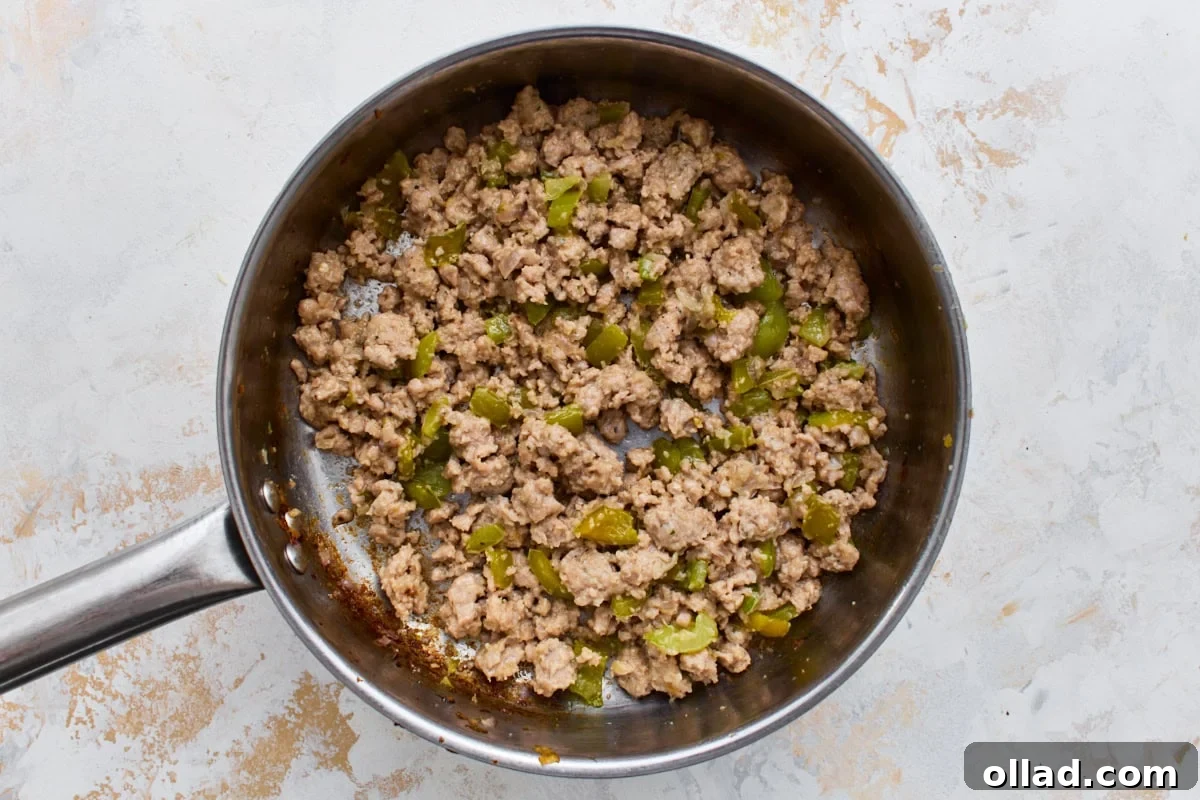 Browned Italian sausage and green bell pepper cooking in a skillet.
