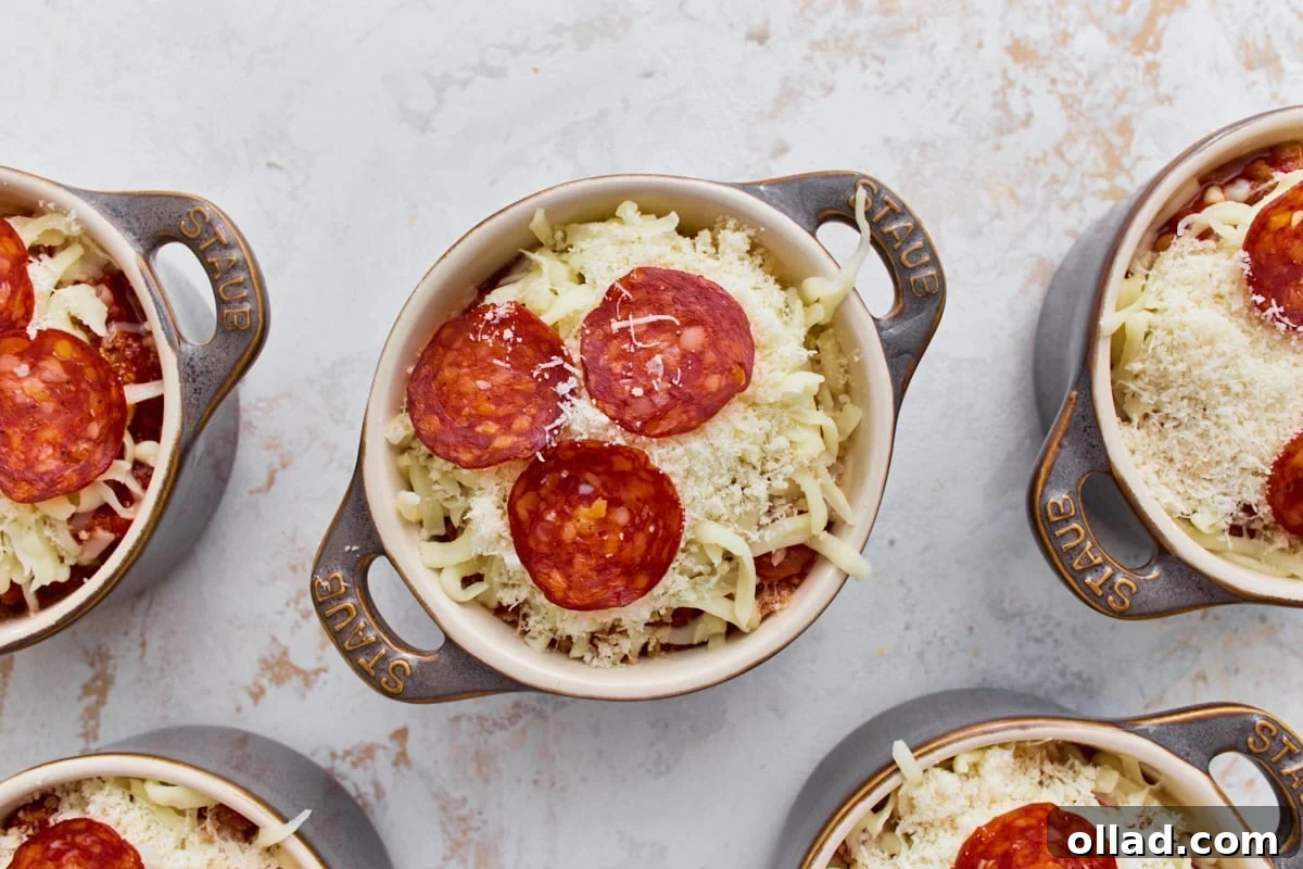 Mini ramekins topped with shredded mozzarella, Parmesan, and pepperoni before baking.