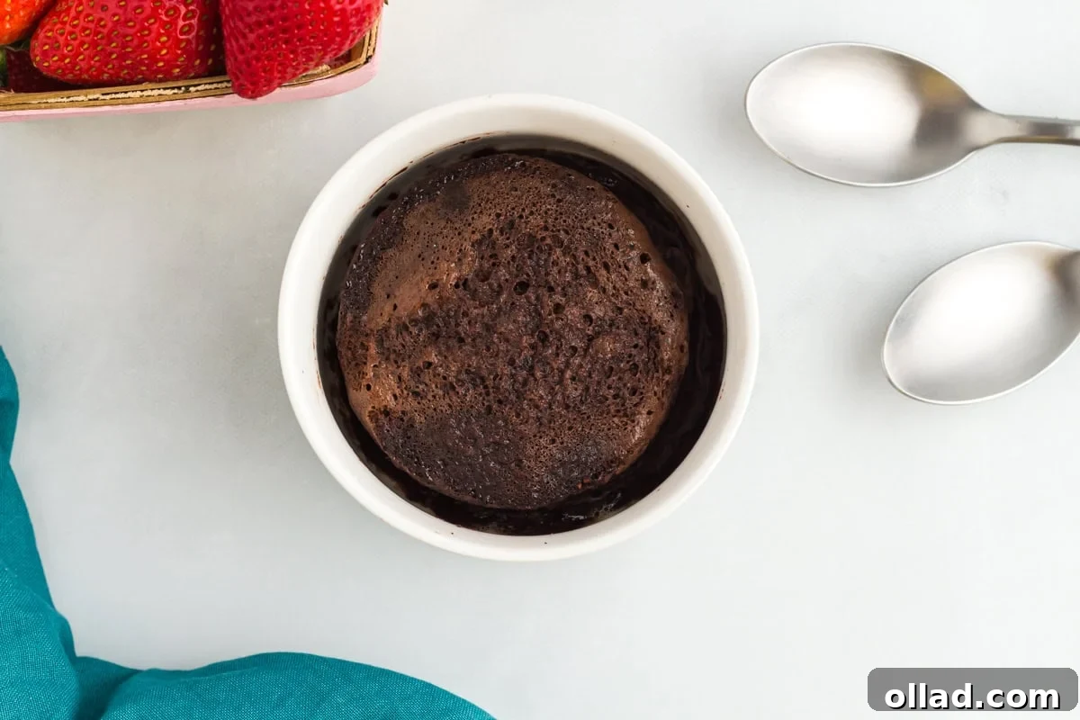 Flourless mug cake in a white ramekin next to fresh strawberries and two spoons